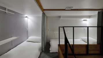 Una habitación de hotel con dos camas individuales, un cabecero de madera, un pequeño estante y una lámpara en el techo.