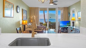 A hotel room with a kitchen area, a dining table, and a large TV. - Stunning 2BR condo in South Kihei with ocean views! (Kihei)
