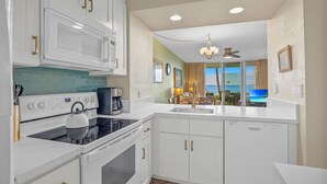 A modern kitchen with white cabinets, a stove, and a sink. There is a view of a balcony with a table and chairs. - Stunning 2BR condo in South Kihei with ocean views! (Kihei)