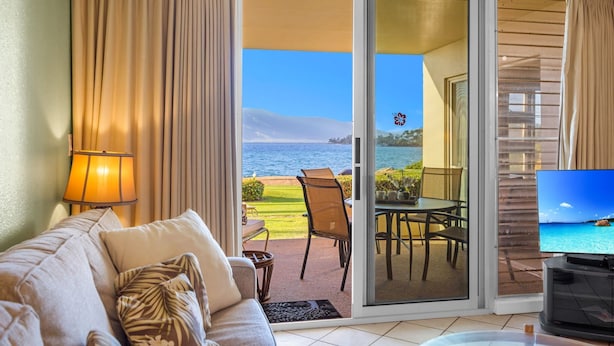 A room with a sofa, a TV, and a view of the ocean through a sliding glass door. - Stunning 2BR condo in South Kihei with ocean views! (Kihei)