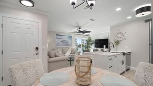 Une cuisine moderne avec un coin repas, comprenant une table ronde avec des sets de table, un ventilateur de plafond et une vue sur l’océan par la fenêtre.