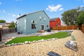 A residential property with a blue house, a red house, a patio with a table and chairs, and a small lawn. - Modern Home | Game Room, Putt Putt & Pets Welcome! (Colorado Springs)