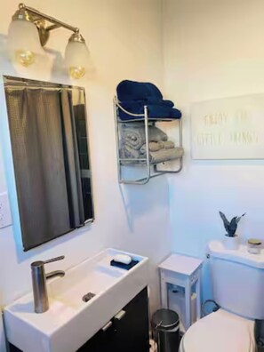 Ein Badezimmer mit weißem Waschbecken, Spiegel, Handtuchhalter, Toilette und Mülleimer.