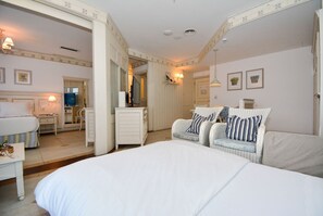 A bedroom with a large bed, two wicker chairs with cushions, a dresser, a television, and a mirror. - IL CAMPANÁRIO (Florianópolis)