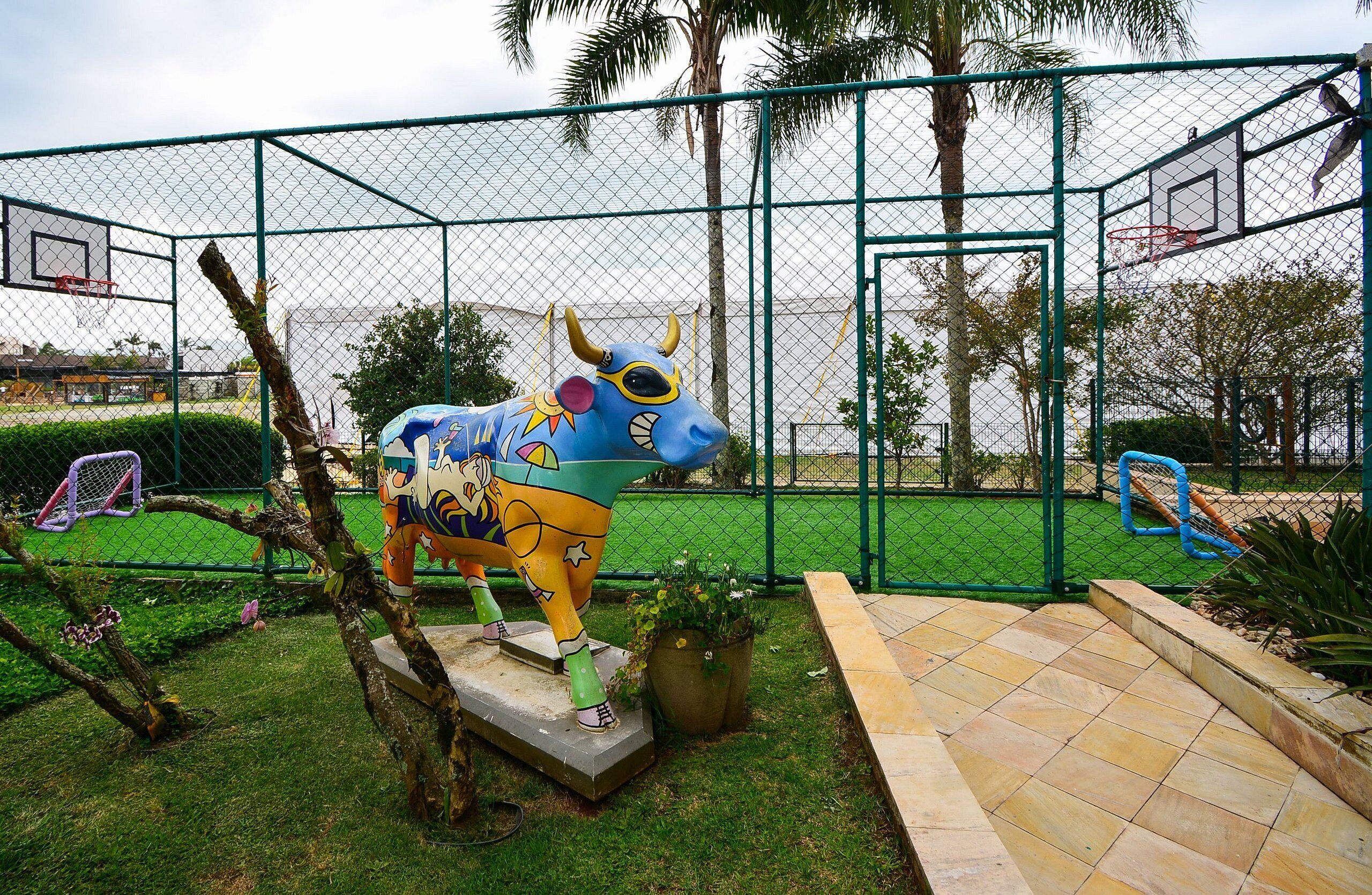 A fenced outdoor area with a colorful bull sculpture, a basketball hoop, and a small garden with potted plants.