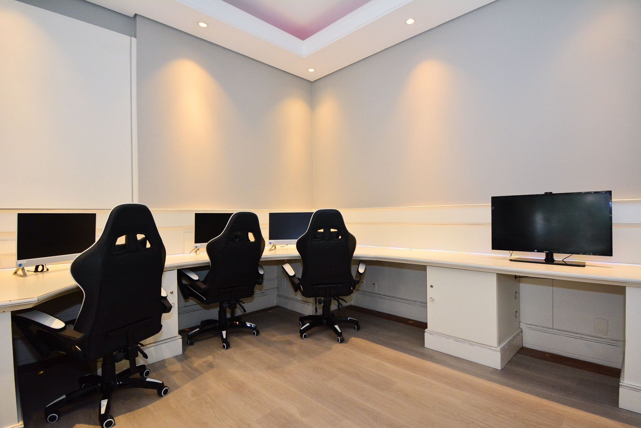 A conference room with three black office chairs, a large flat-screen TV, and a white desk.