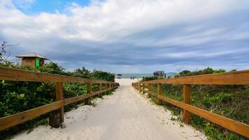 A wooden boardwalk leading to a beach with a small structure on the left.