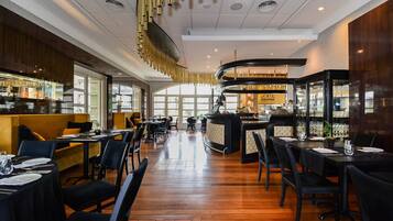 A restaurant with a bar area, wooden flooring, and a modern ceiling design.