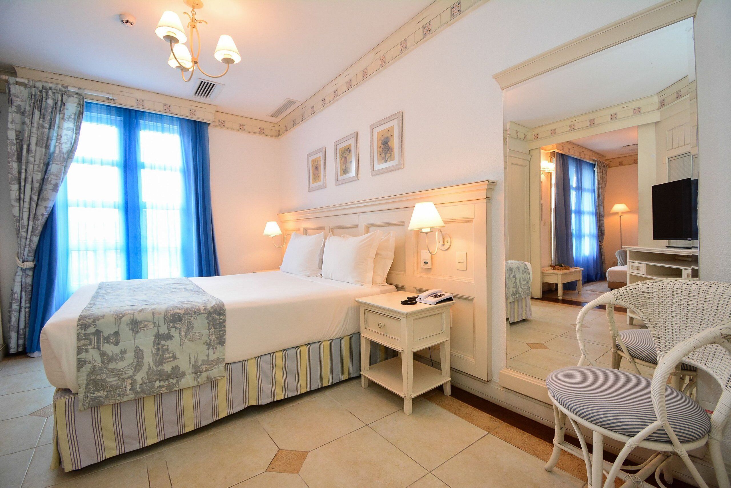 A hotel room with a bed, bedside table, chair, and a mirror.