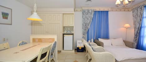 A compact room with a dining table, chairs, a bed, and a small kitchenette.