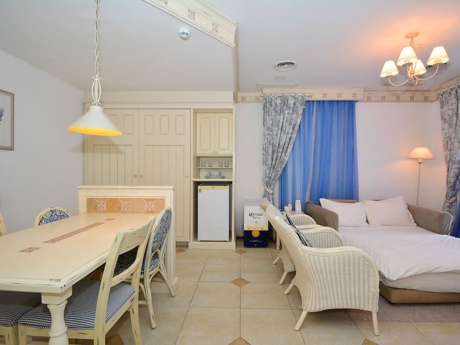 A compact room with a dining table, chairs, a bed, and a small kitchenette.