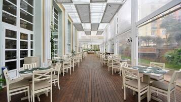 A covered outdoor dining area with wooden flooring and white furniture.
