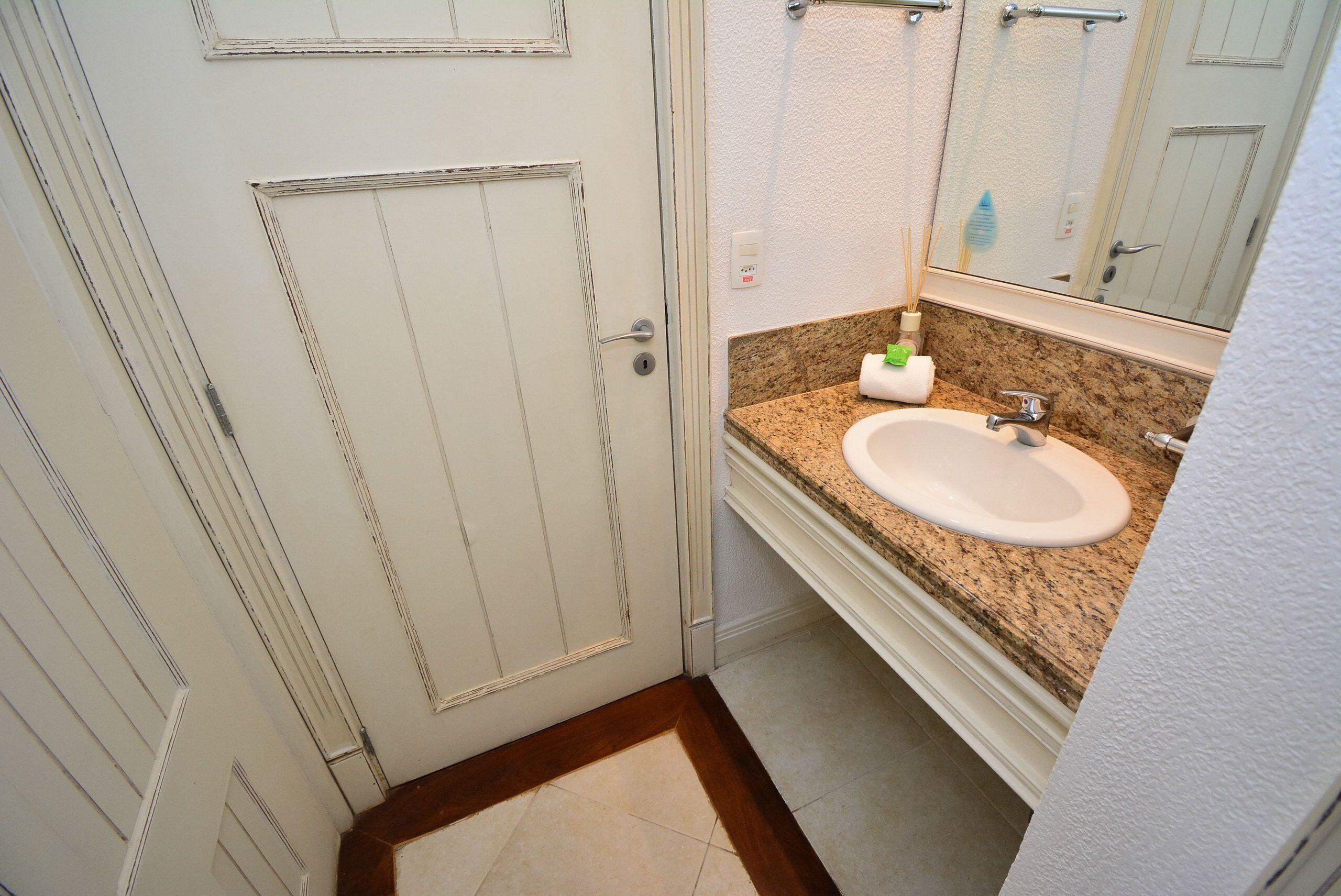 A bathroom with a white door, a sink with a granite countertop, and a mirror above the sink.