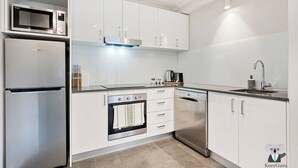 A modern kitchen with white cabinets, a built-in microwave, a refrigerator, an oven, a dishwasher, and a stainless steel sink. - KozyGuru | Darlinghurst | Chic Studio by Hyde Park (Darlinghurst)
