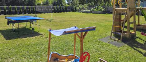 Un jardin avec un bac à sable, une table de ping-pong et une structure de jeu en bois.