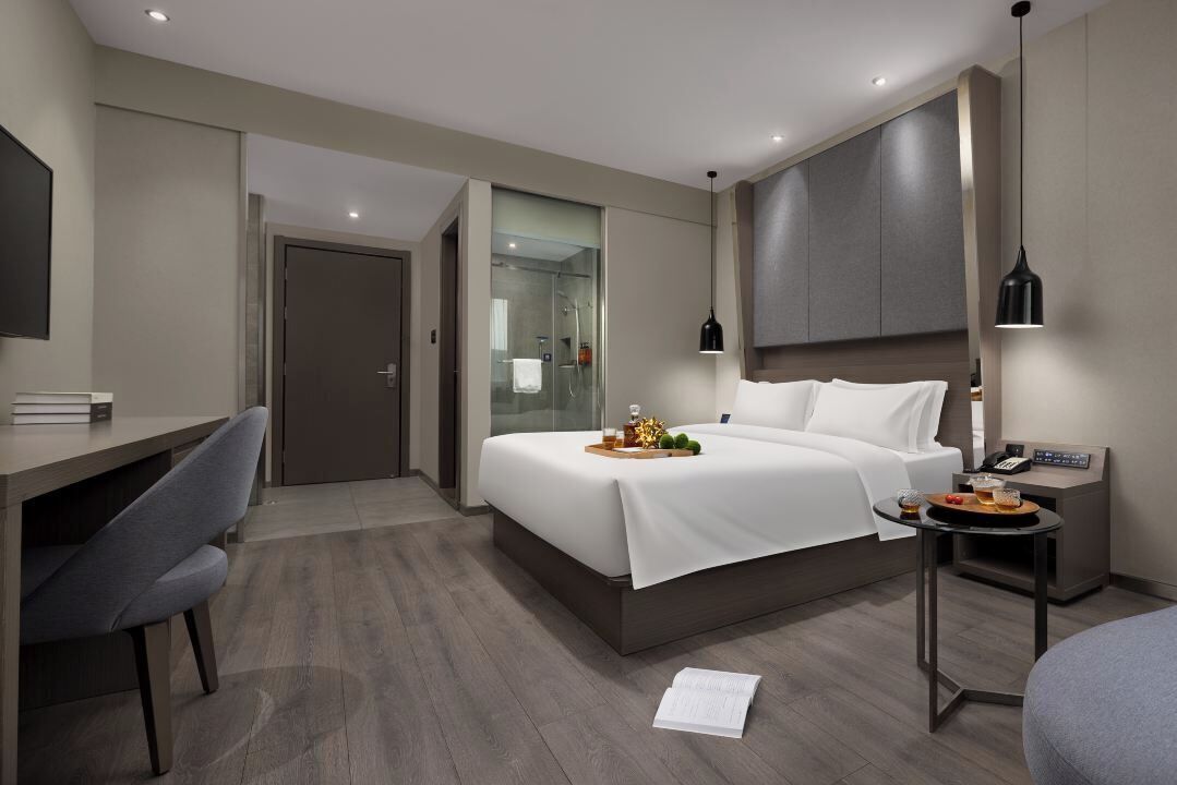 Ein modernes Hotelzimmer mit Bett, Nachttisch, Schreibtisch, Stuhl und einer Dusche.