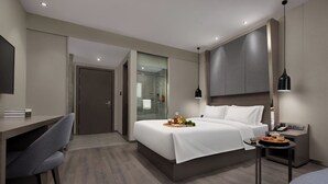 Ein modernes Hotelzimmer mit Bett, Nachttisch, Schreibtisch, Stuhl und einer Dusche.