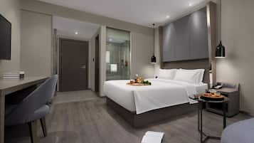 Ein modernes Hotelzimmer mit Bett, Nachttisch, Schreibtisch, Stuhl und einer Dusche.