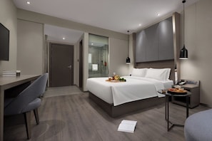 Ein modernes Hotelzimmer mit Bett, Nachttisch, Schreibtisch, Stuhl und einer Dusche.