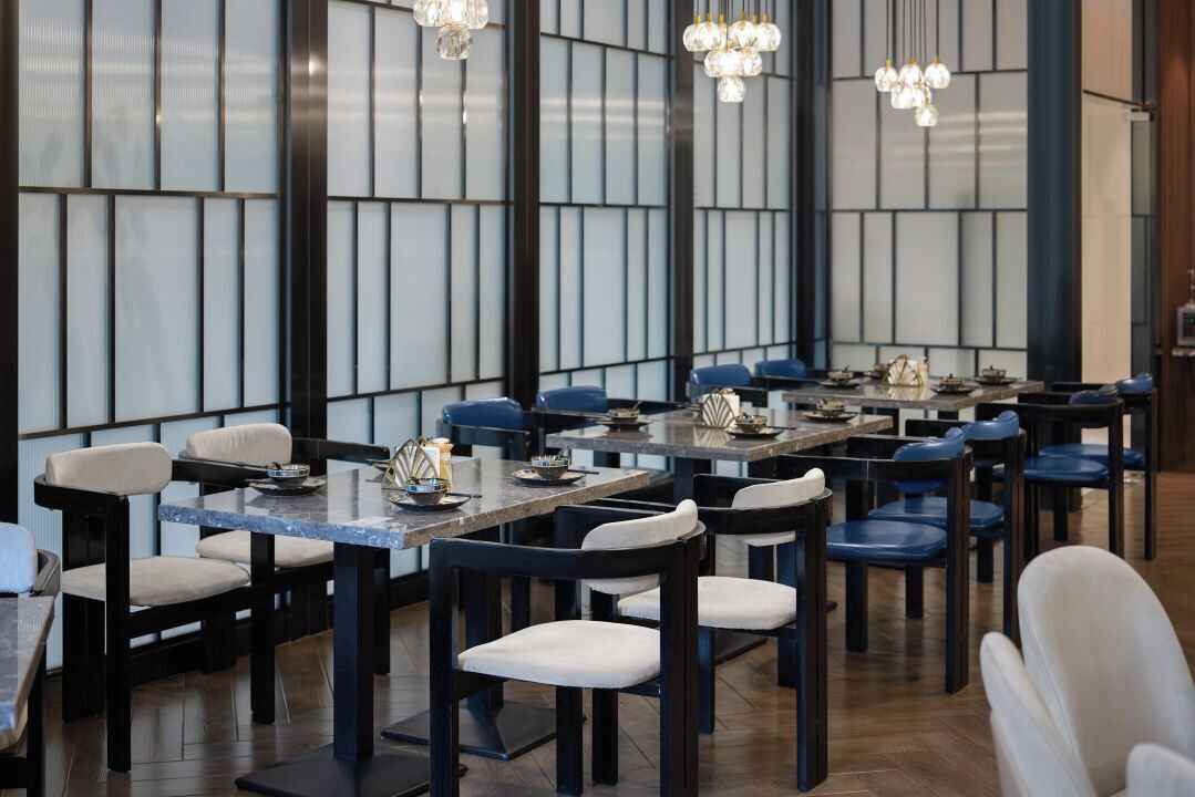 A modern dining area with multiple tables and chairs, featuring a contemporary design with dark wood furniture and light-colored cushions.