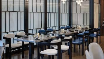 A modern dining area with multiple tables and chairs, featuring a contemporary design with dark wood furniture and light-colored cushions.