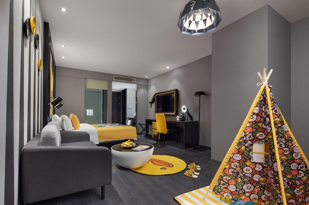 A modern hotel room with a bed, sofa, desk, and a colorful teepee.