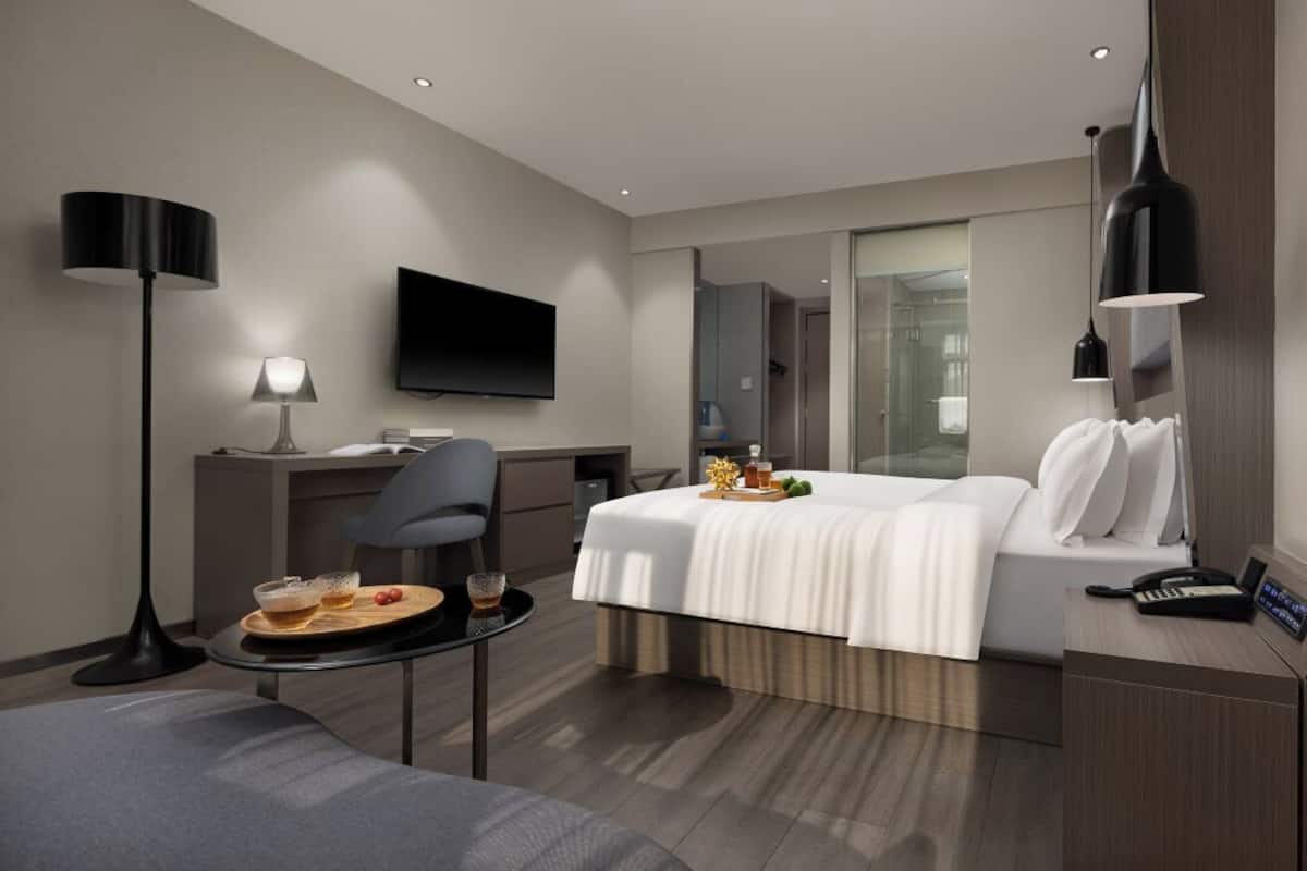 Une chambre d’hôtel moderne équipée d’un lit, d’un bureau, d’une chaise, d’une télévision et d’une petite table sur laquelle se trouve un plateau avec de la nourriture.