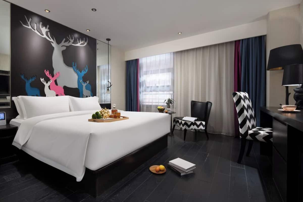 Une chambre d’hôtel moderne avec un grand lit, un bureau, une chaise et une fresque murale.