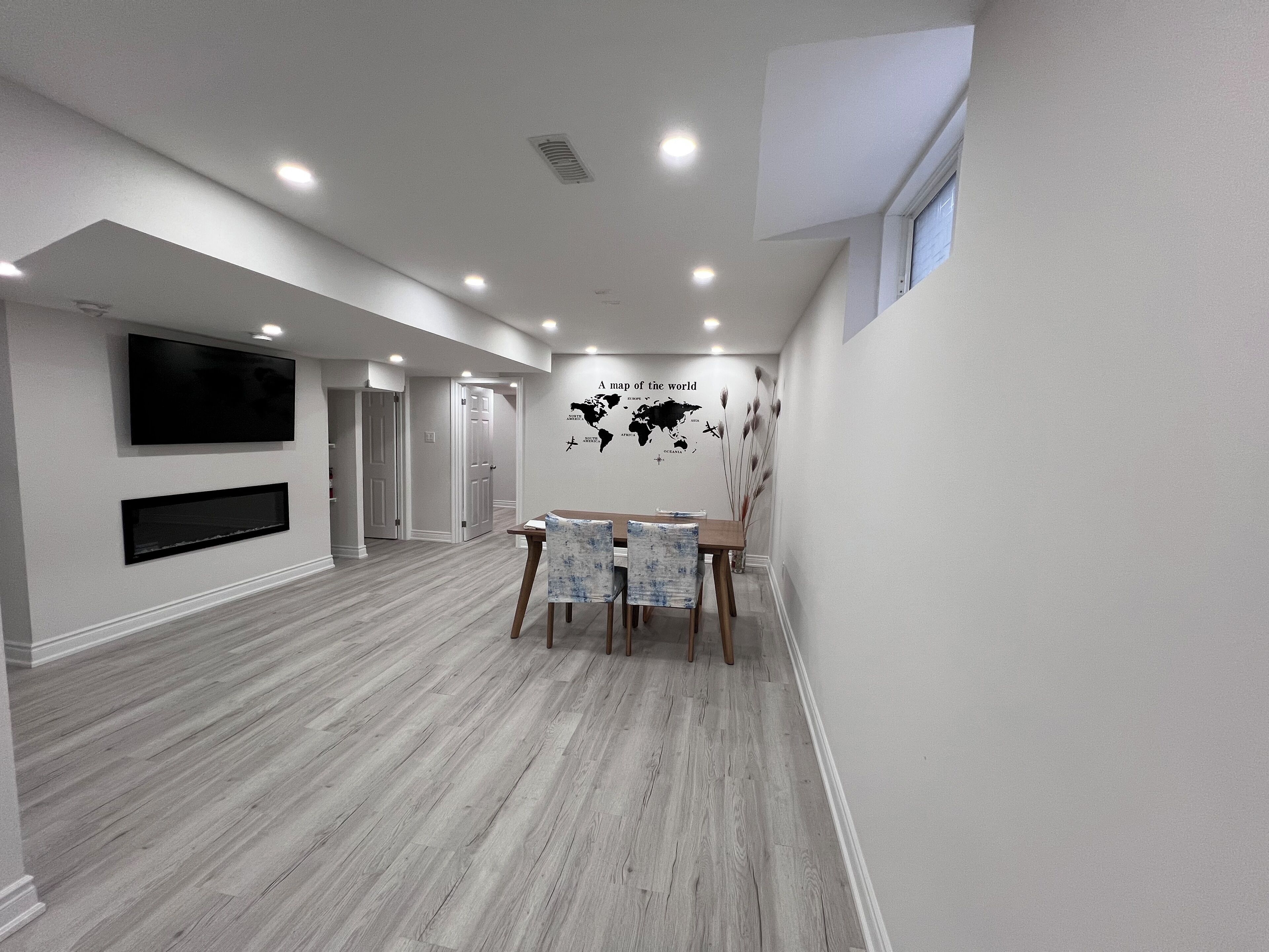 A spacious room with a wooden floor, a dining table with chairs, a flat-screen TV mounted on the wall, and a world map decoration.