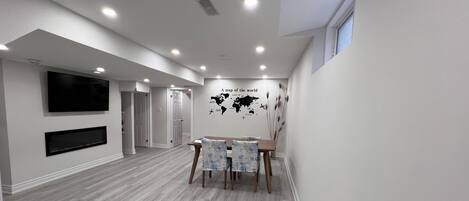 A spacious room with a wooden floor, a dining table with chairs, a flat-screen TV mounted on the wall, and a world map decoration.