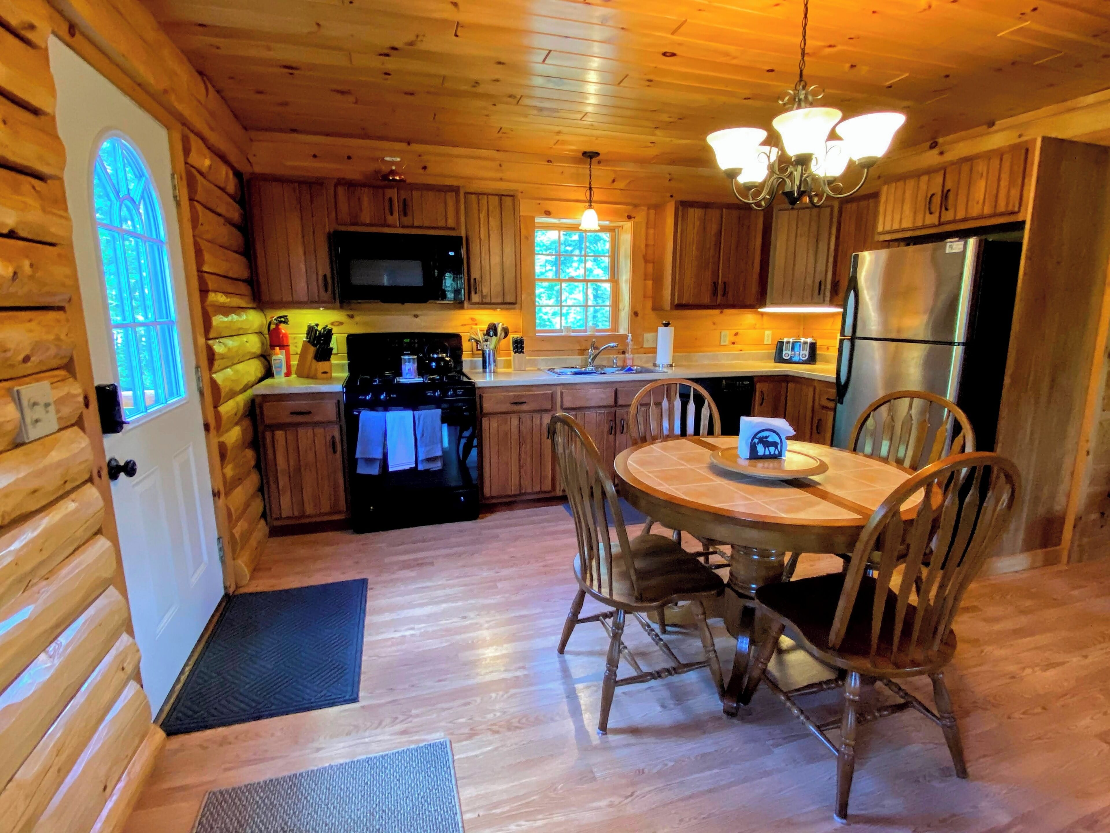 Une cuisine rustique aménagée dans une cabane en bois, équipée d’une cuisinière, d’un four à micro-ondes, d’un réfrigérateur et de meubles de rangement en bois.