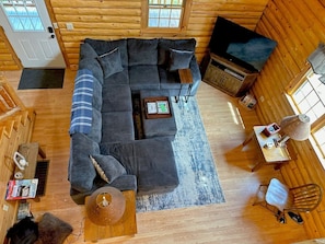 A cozy log cabin interior with a sectional sofa, a television, and a small table with a lamp. - 40pl Log Cabin With AC in the Heart of the White Mountains, Less Than 10 Minutes From Bretton Woods! (Twin Mountain)