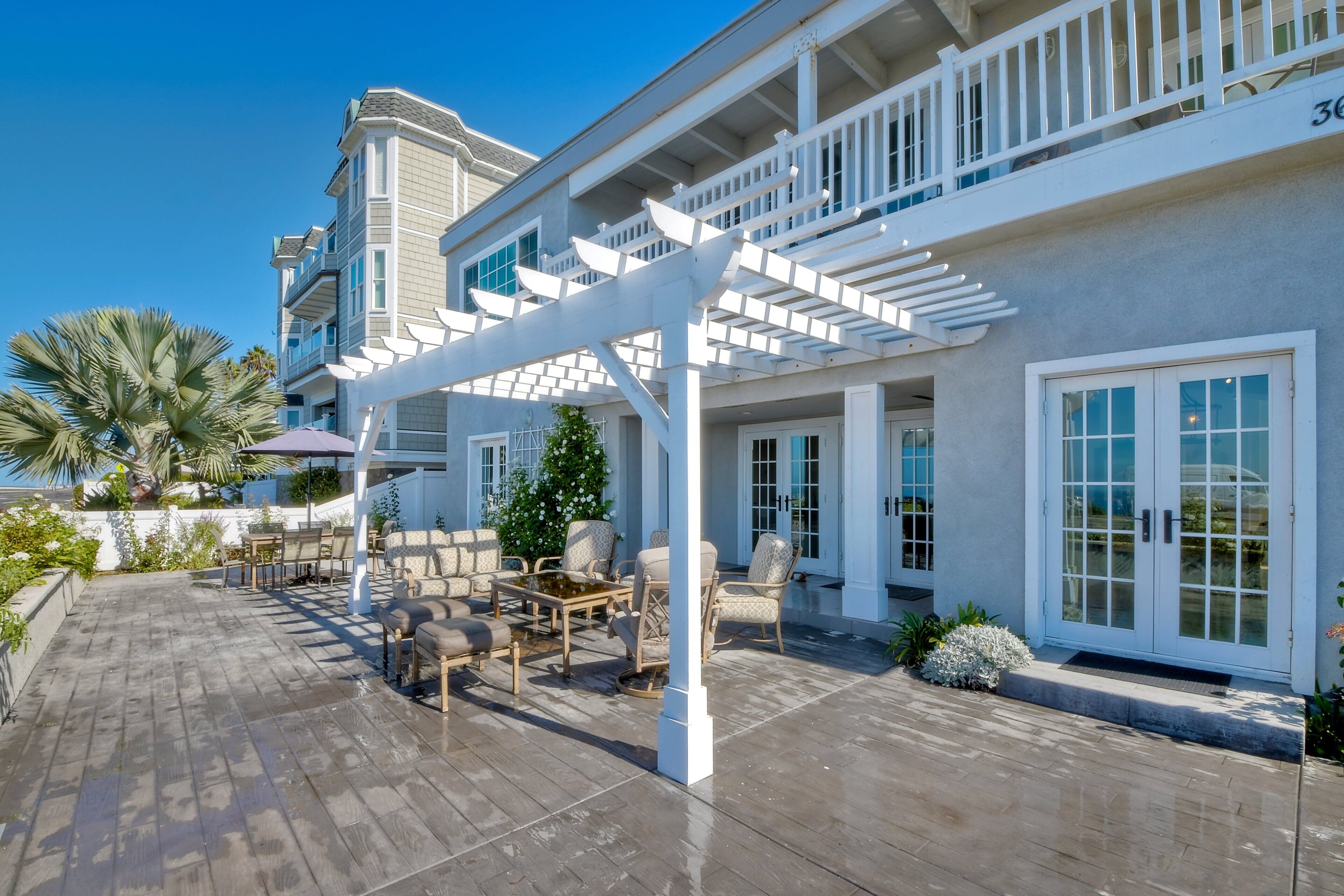 A covered outdoor patio with furniture, a pergola, and a building with large windows and a balcony.