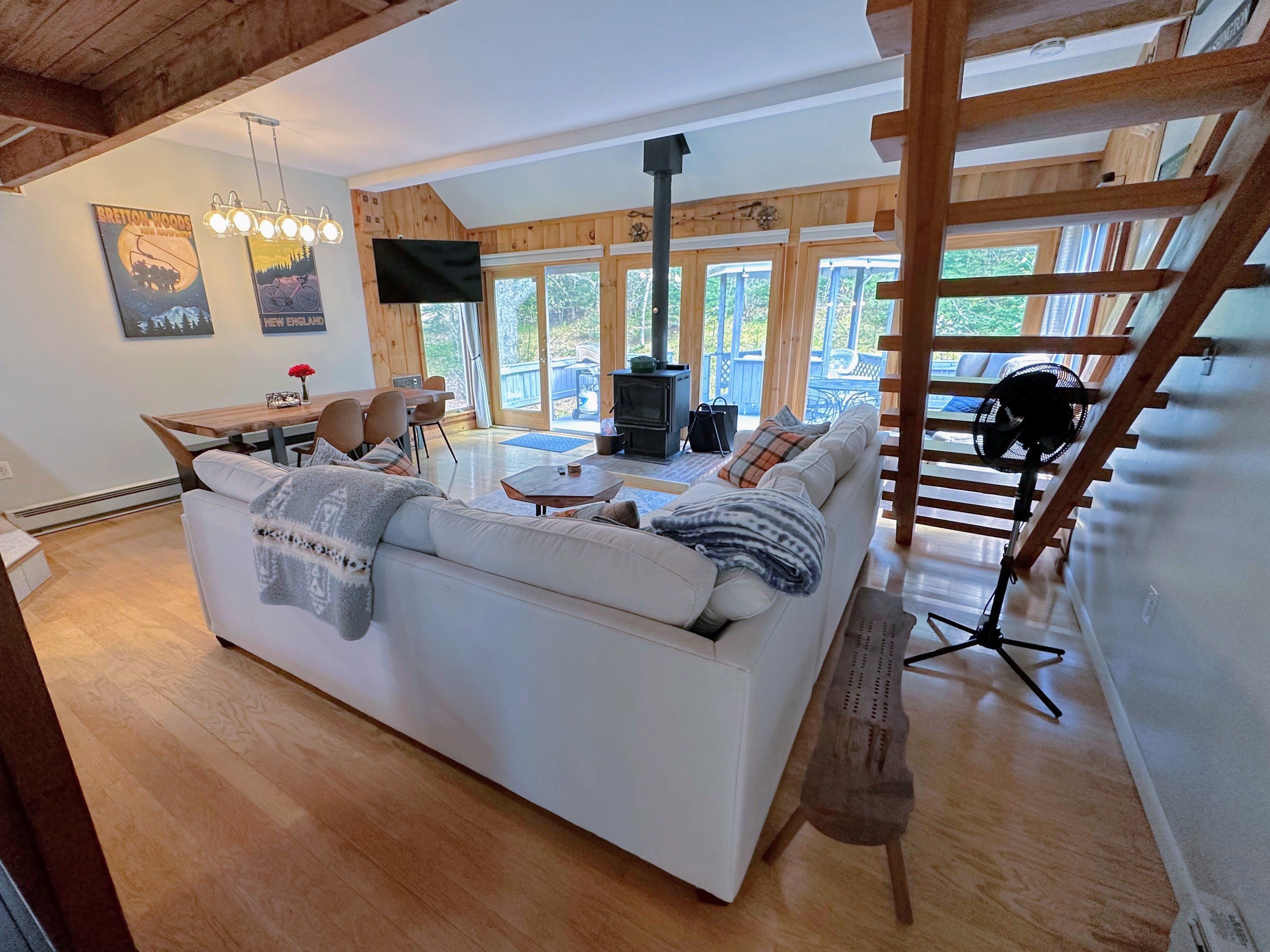 A cozy living room with a white sofa, wooden beams, a fireplace, and large windows.