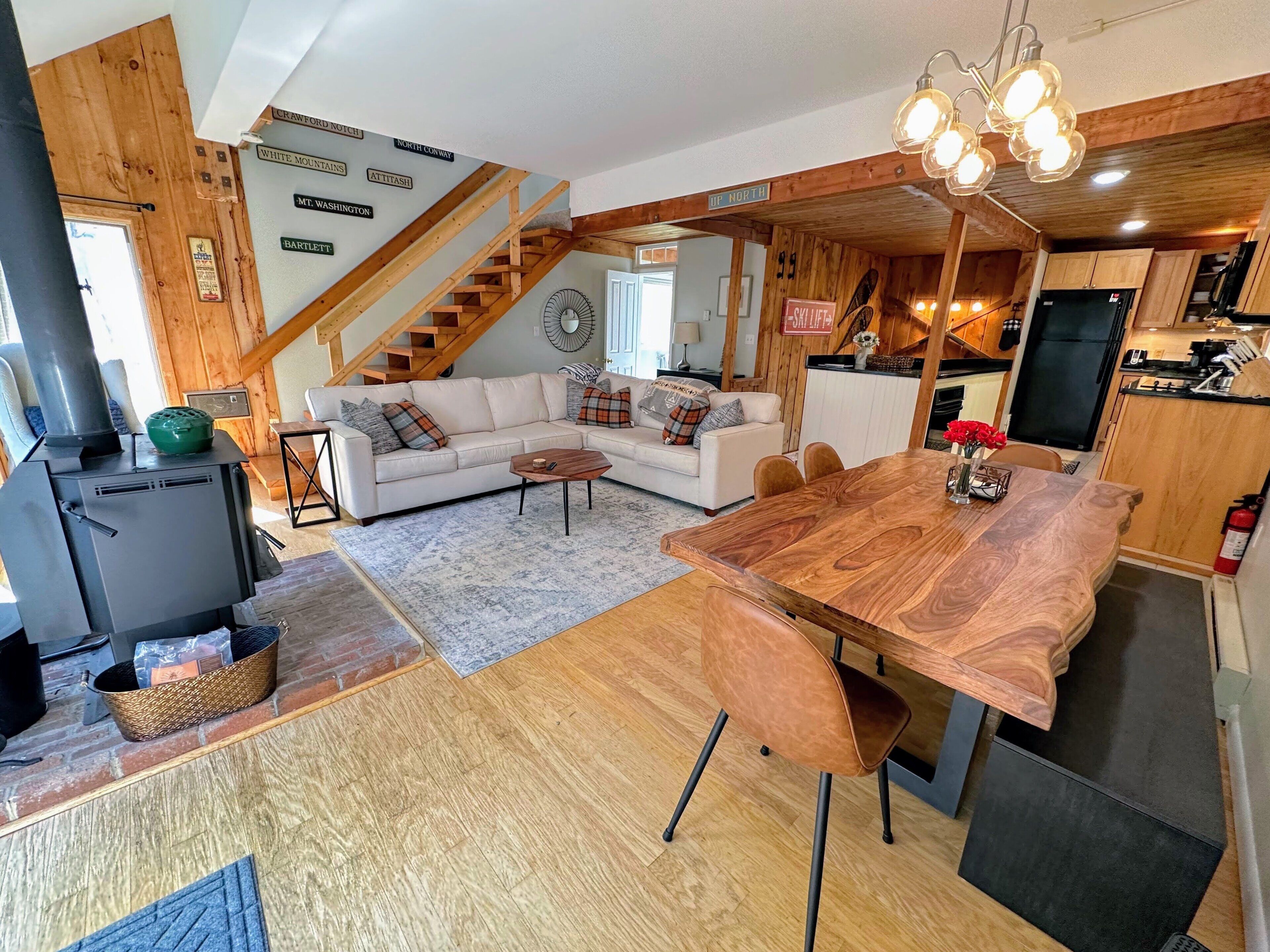 A cozy cabin interior with a living area, wooden staircase, and a kitchen.