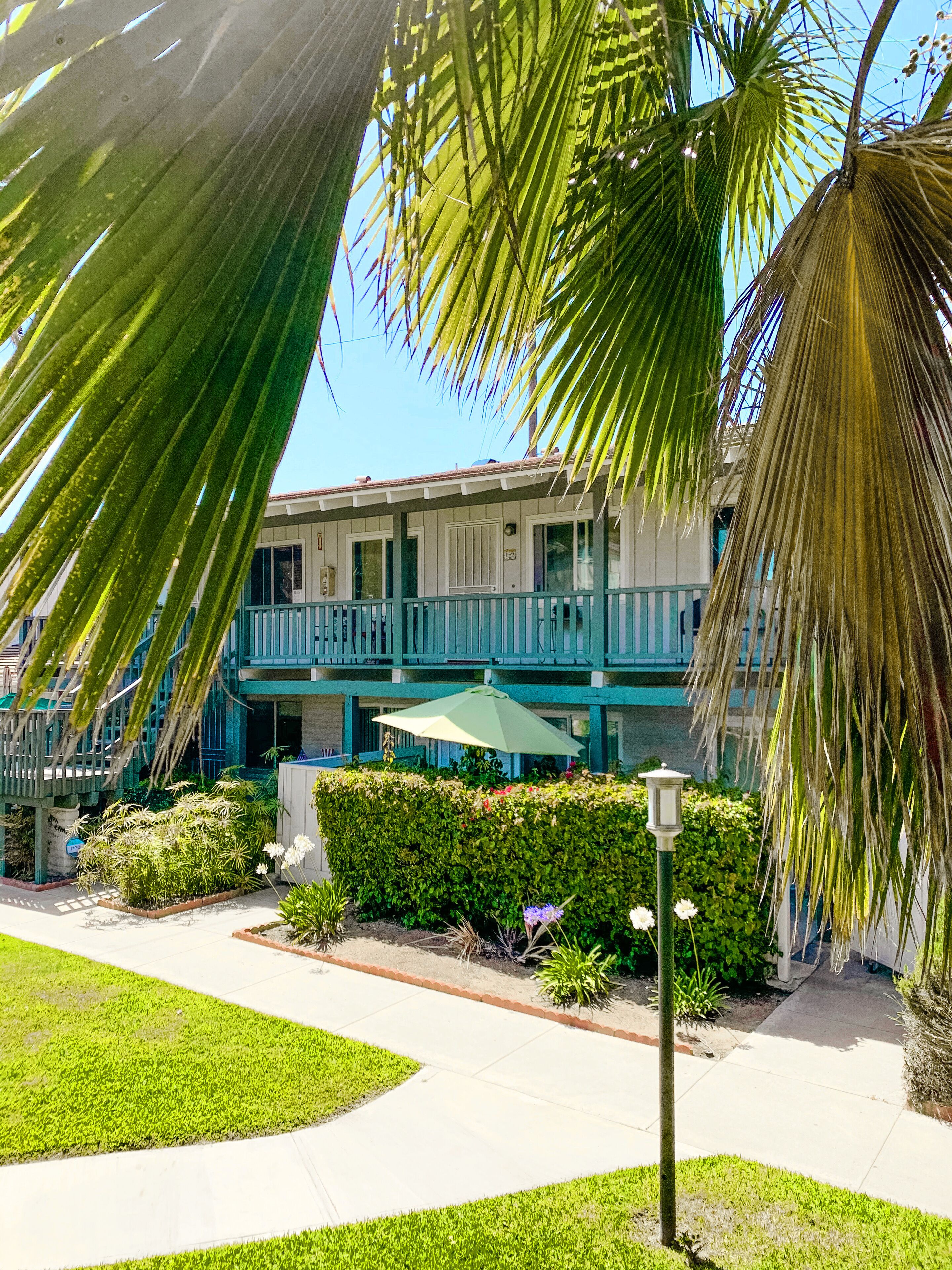 A building with a balcony, surrounded by well-maintained gardens and palm trees.