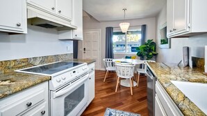 A modern kitchen with white cabinets, a granite countertop, a built-in oven, and a dining area with a white table and chairs. - 3080 Lincoln - Unit 12 (Carlsbad)