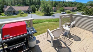 Een terras met een barbecue, een stoel en een tafel. Achtergrond: huizen en een weg.