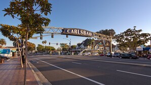 Ein Straßenschild mit der Aufschrift 'CARLSBAD', im Hintergrund eine freie Straße und Gebäude.