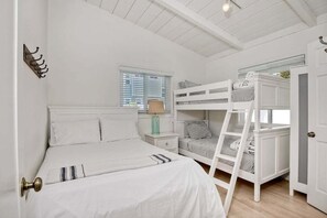 Una camera da letto con un letto a castello, un letto singolo, un comodino con una lampada e una finestra con persiane.