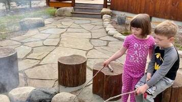 Una cabaña de madera con un patio de piedra, un brasero y una terraza de madera.