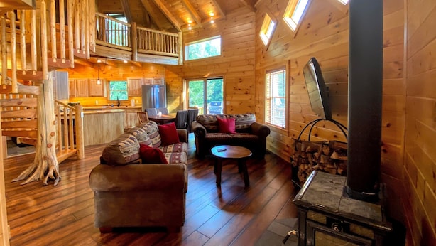 A log cabin interior with a wooden staircase, a living room with a sofa and chairs, a kitchen area, and a fireplace. - 1800or Unique 'yurt' Home in Bretton Woods 1 mi to Skiing, Firepit, Foosball, Beach! Hot tub (Bretton Woods)