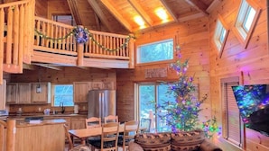 A cozy cabin interior with a dining area, a living room with a sofa, a Christmas tree, and a TV. - 1800or Unique 'yurt' Home in Bretton Woods 1 mi to Skiing, Firepit, Foosball, Beach! Hot tub (Bretton Woods)