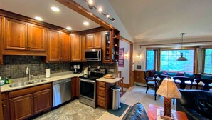 Una cucina moderna con mobili in legno, elettrodomestici in acciaio inossidabile e un'area pranzo con un divano in pelle nera e una lampada da tavolo.