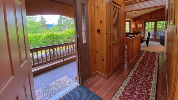 Ambiente interno in legno con una porta che dà su un balcone, un tappeto decorato e vista sul verde circostante.