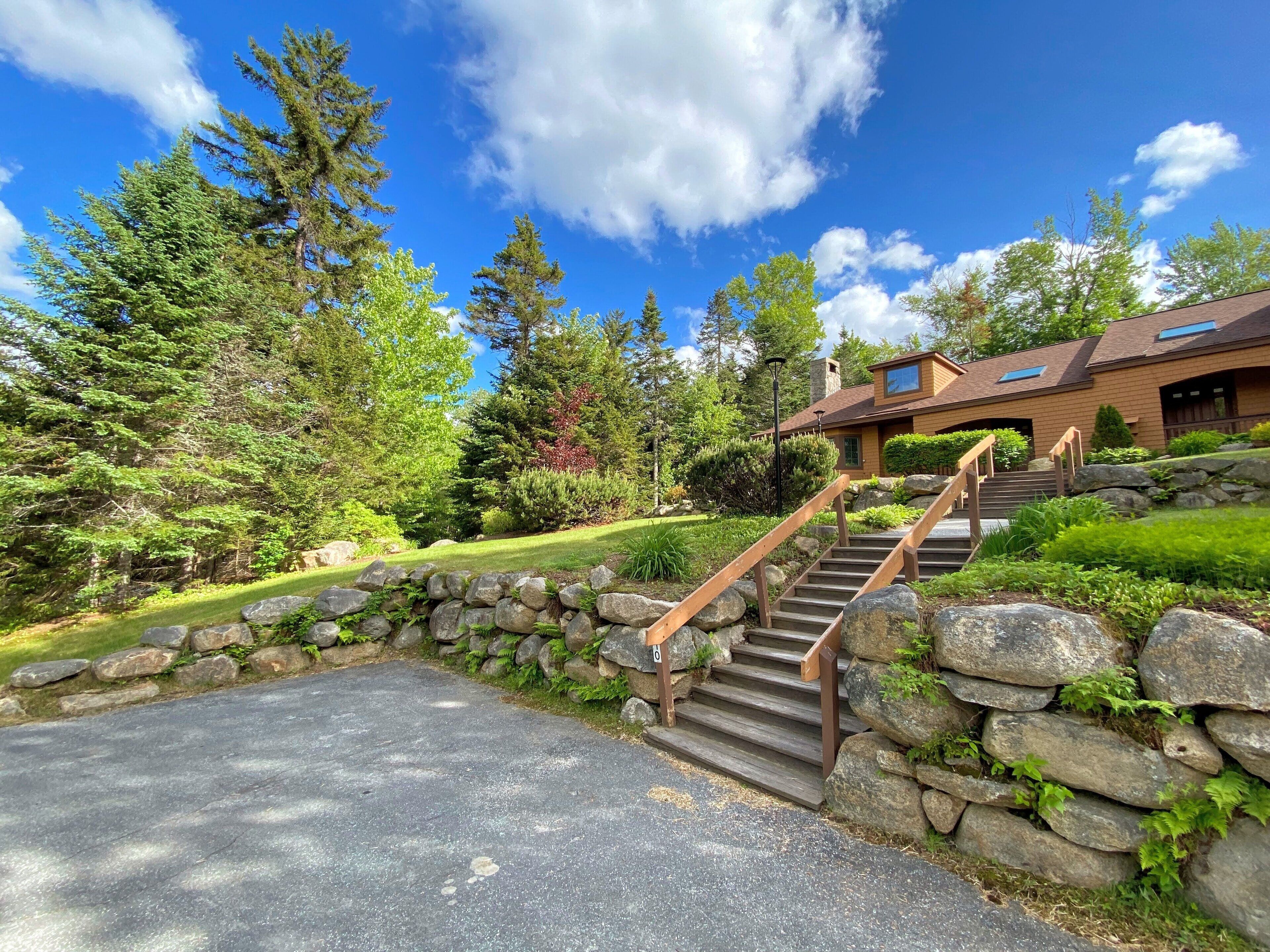 A house with a stone staircase leading to a wooden deck, surrounded by lush greenery and trees.