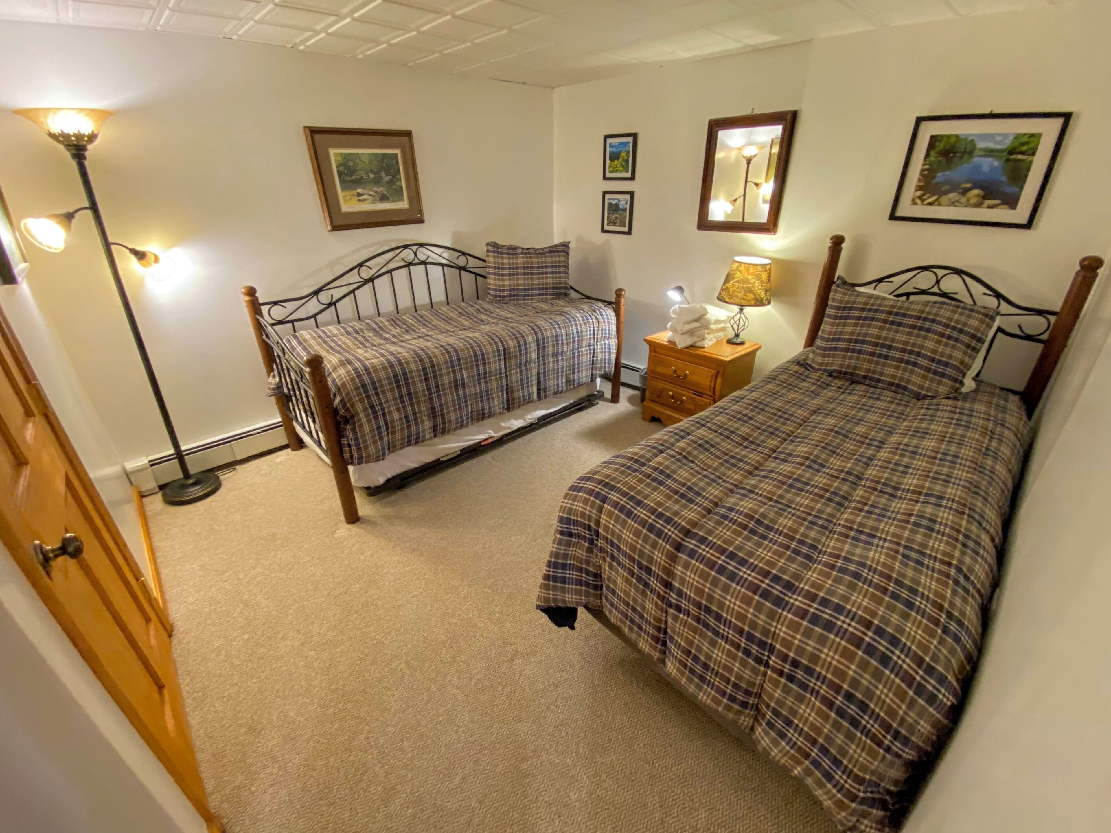 A bedroom with two beds, a nightstand, a lamp, and framed pictures on the walls.