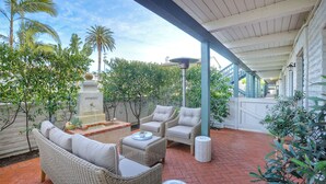 Une terrasse couverte aménagée avec des meubles en osier, une petite fontaine et une végétation luxuriante.