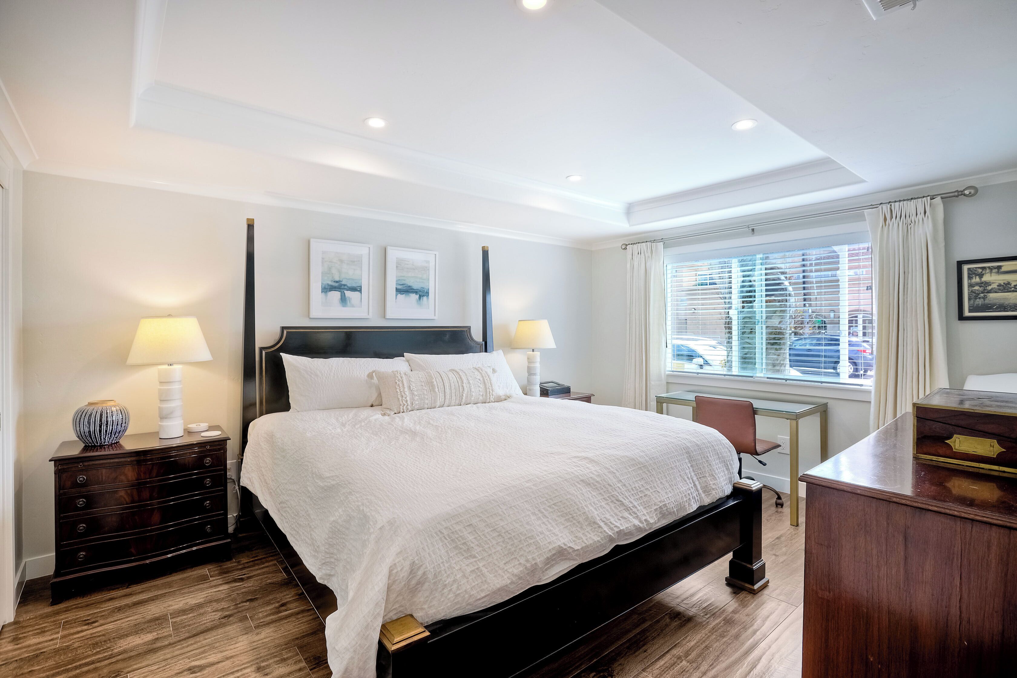 A neatly arranged bedroom with a large bed, bedside tables, a desk, and a window with curtains.