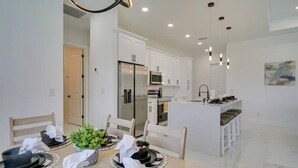 A modern kitchen with white cabinetry, a central island, and a dining area with a table set for four. - 290) Perfect for Families! (Cape Coral)